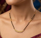 Necklace with black and gold beads on a person wearing a maroon saree.