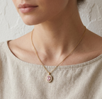 Necklace with a pink pendant worn by a person in a beige top against a neutral background