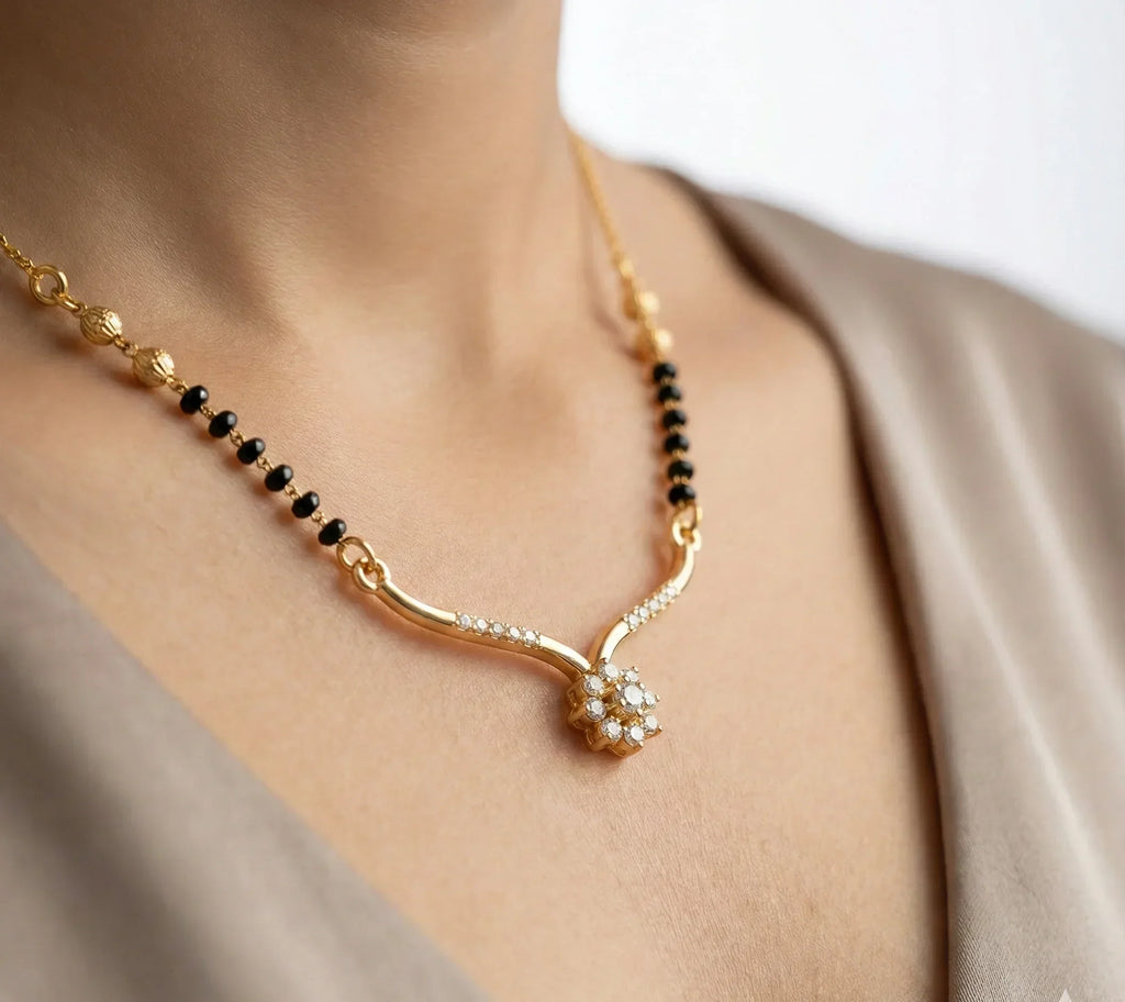 Gold necklace with black beads and a floral pendant on a person wearing a beige top.