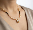 Gold necklace with black beads and a floral pendant on a person wearing a beige top.