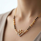Gold necklace with black beads and leaf design on a person wearing a beige top.