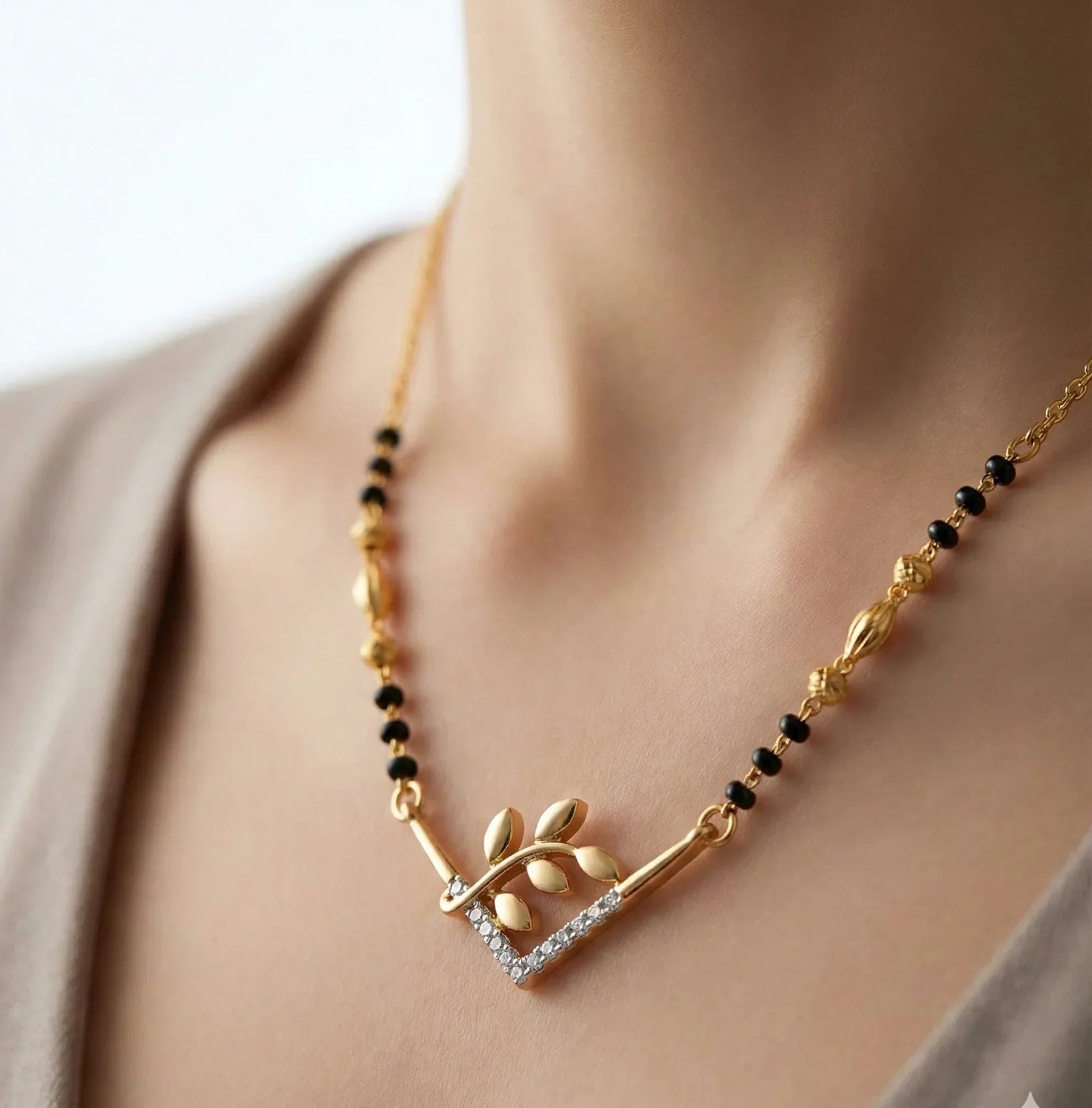 Gold necklace with black beads and leaf design on a person wearing a beige top.