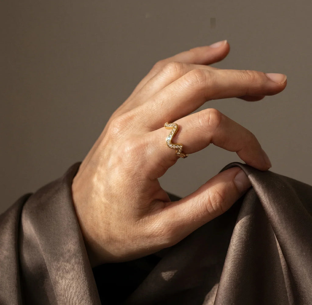 Hand wearing a gold ring on a brown fabric background