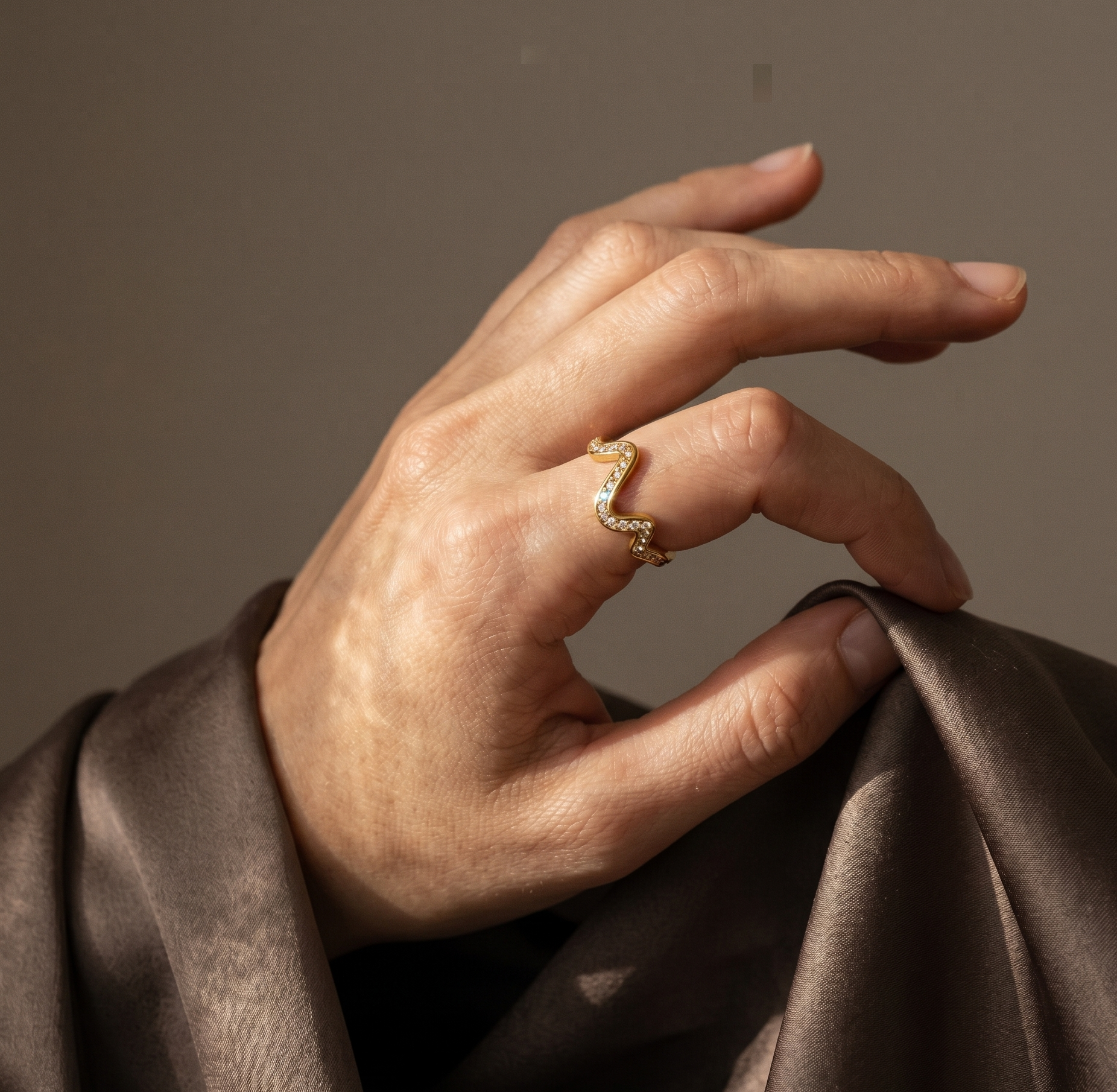 Hand wearing a gold ring on a brown fabric background