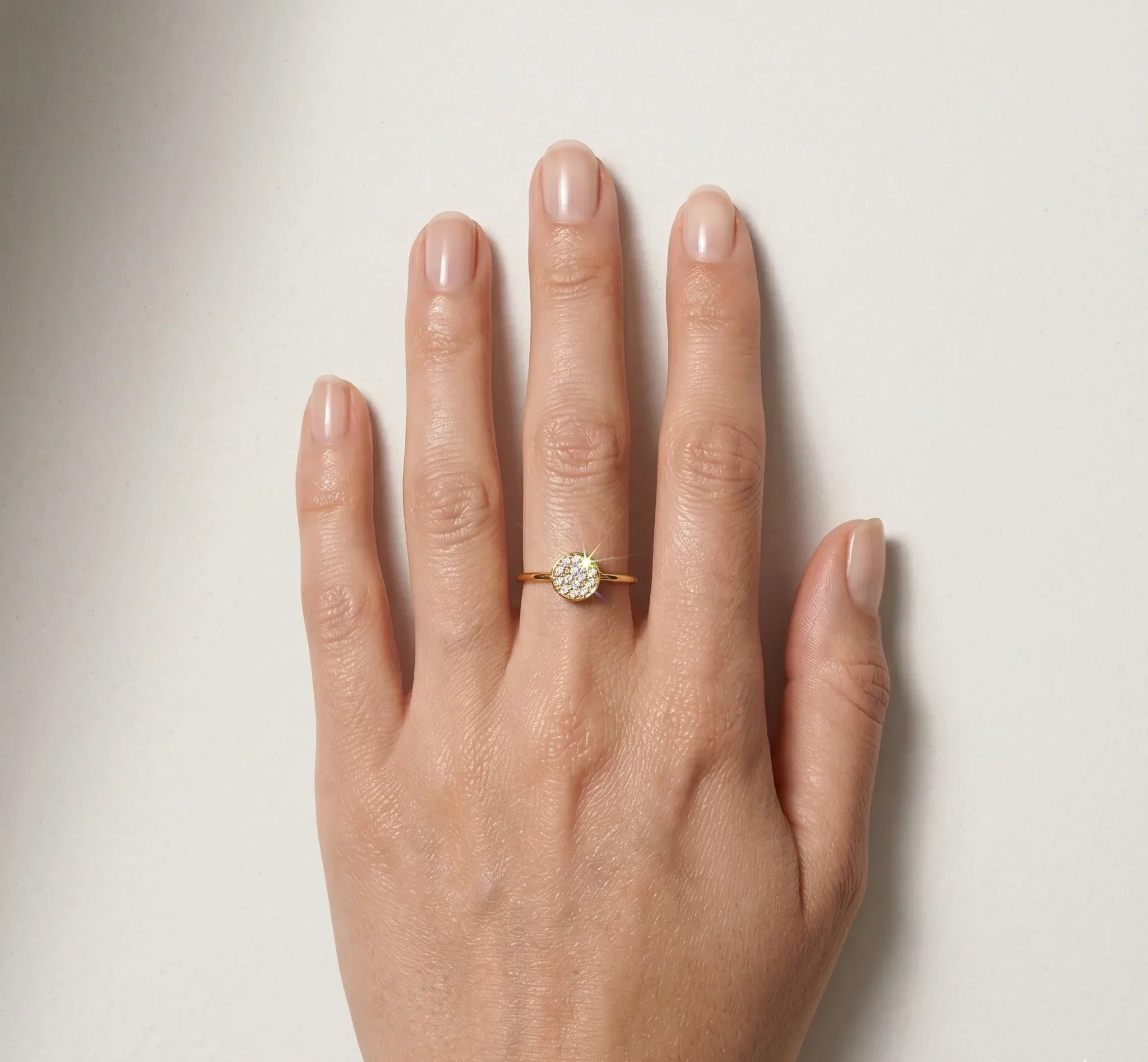 Hand wearing a gold ring with a diamond on a light background