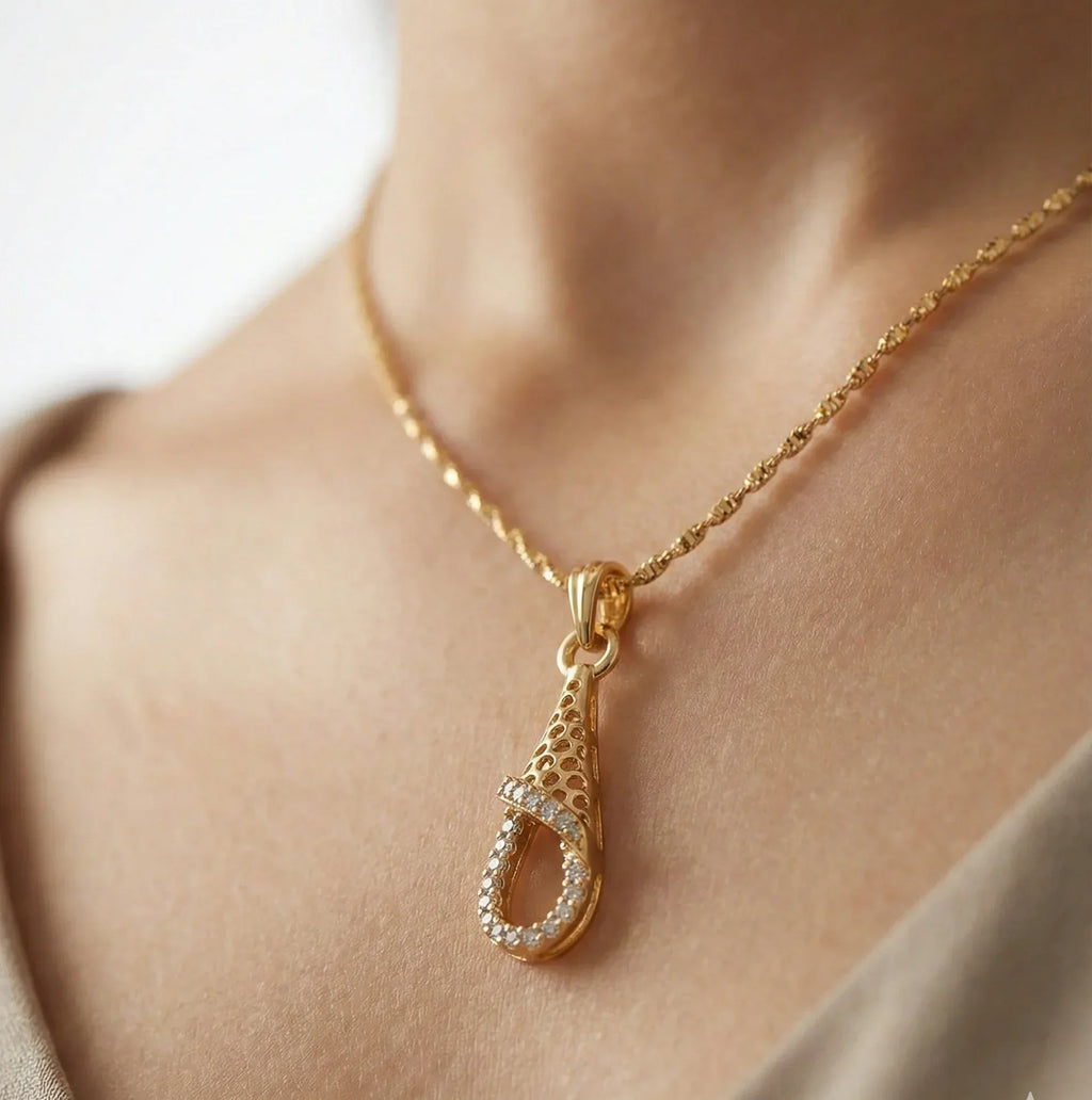 Gold necklace with a teardrop pendant on a person's neck against a neutral background