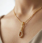 Gold necklace with a teardrop pendant on a person's neck against a neutral background