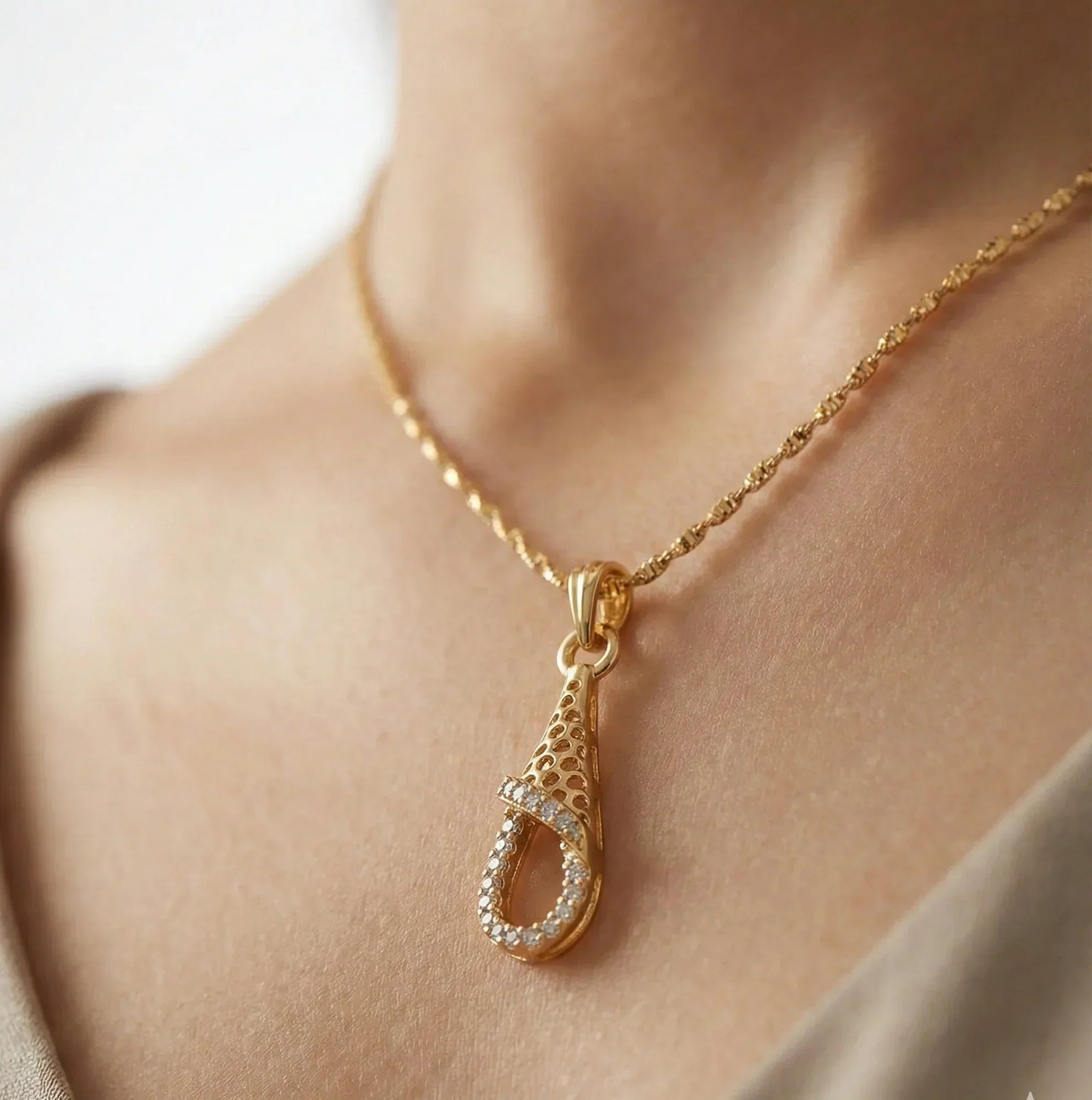 Gold necklace with a teardrop pendant on a person's neck against a neutral background