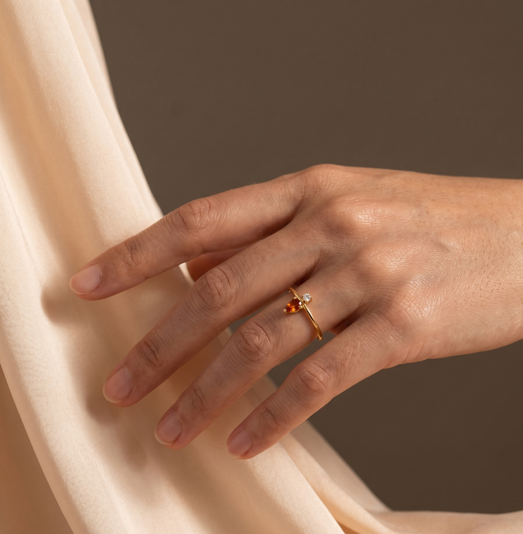 Hand wearing a gold ring with a red gemstone on a beige fabric background