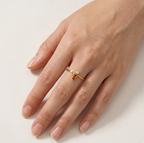 Hand wearing a gold ring with a gemstone on a light background