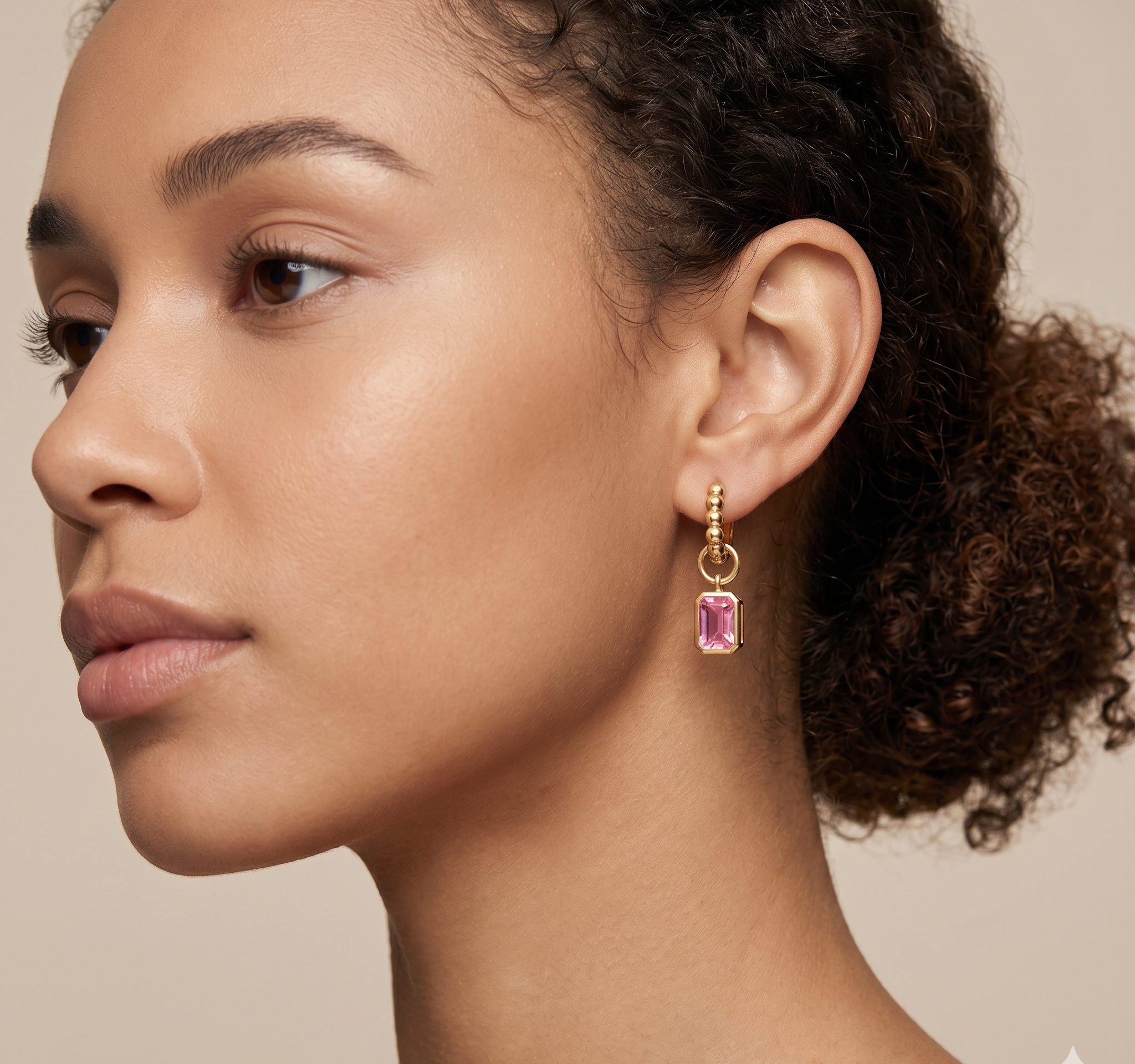 Close-up of a woman wearing pink gemstone earrings with gold hooks on a beige background
