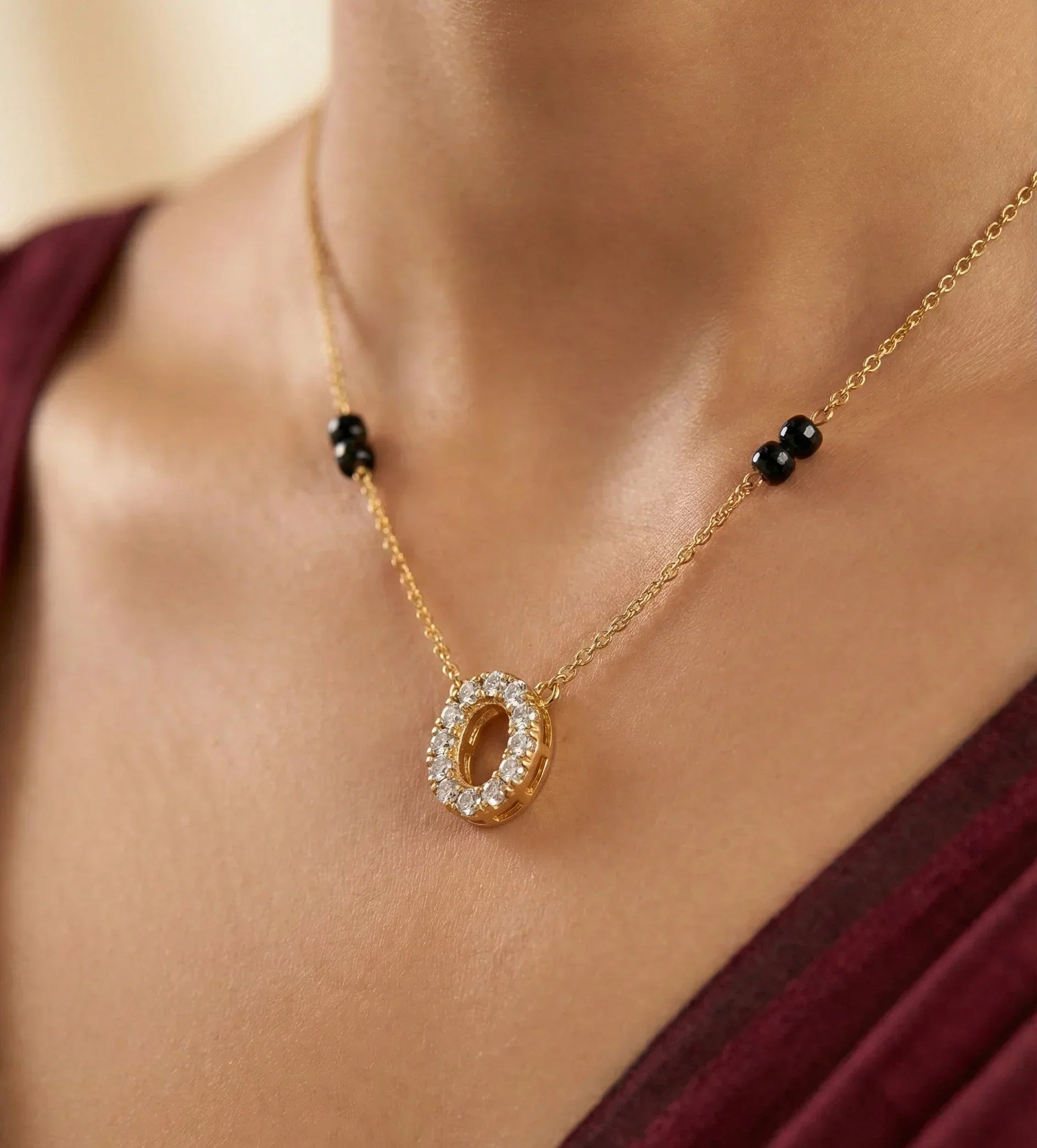 Gold necklace with a circular pendant worn by a person in a burgundy top.