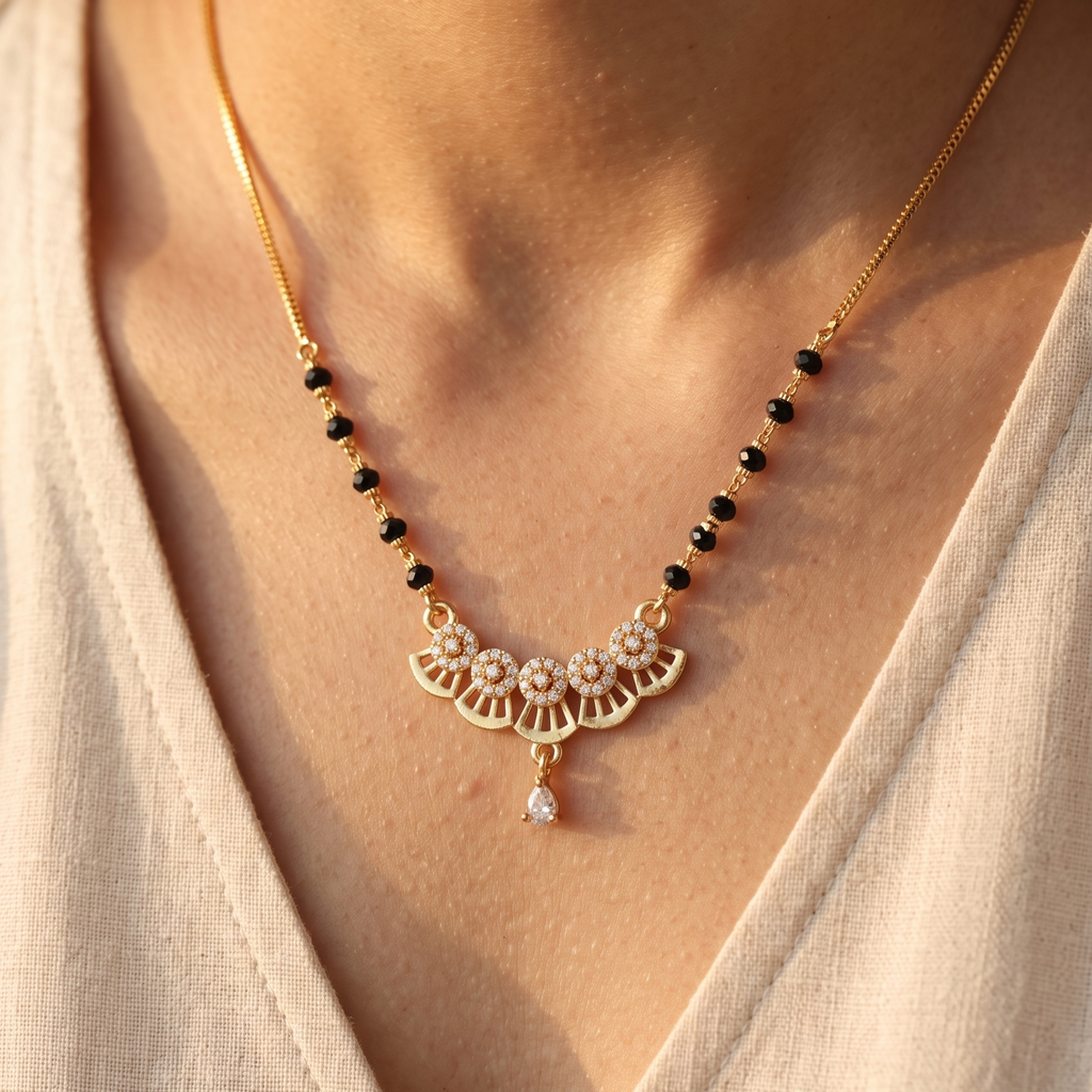 A gold chain necklace with small black beads and a central fan-shaped pendant set with clear stones, worn on a model's neck.