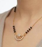 Gold necklace with black beads on a person wearing a beige top.