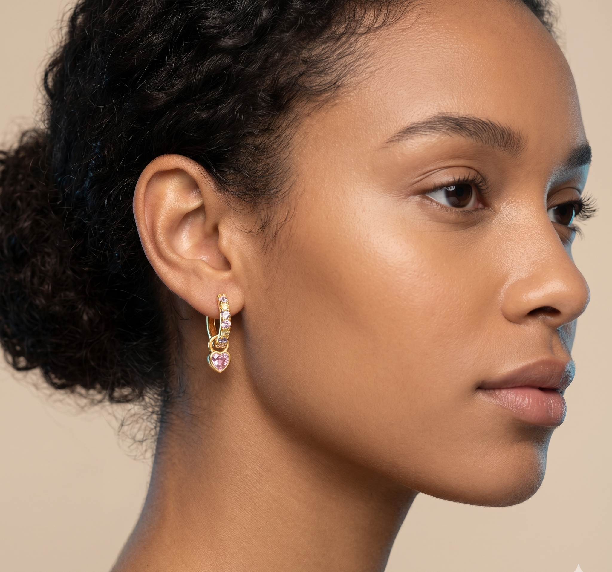 Close-up of a woman wearing a gold earring with pink gemstones on a beige background
