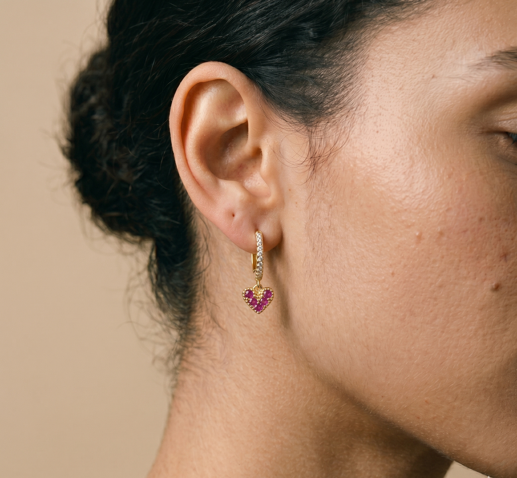 Close-up of a person wearing a gold earring with pink gemstones on a beige background