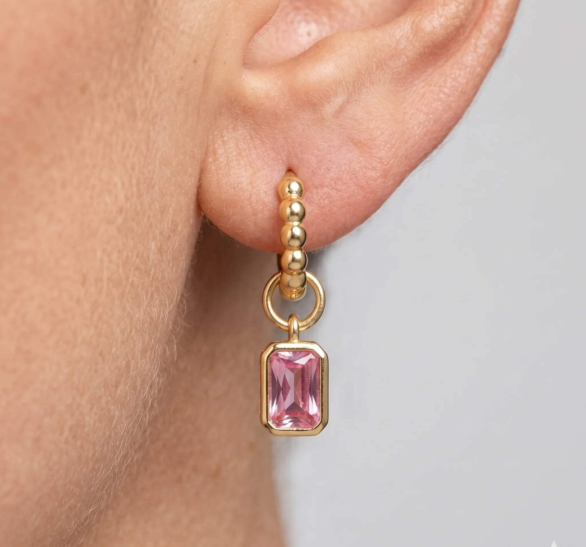 Gold earring with pink gemstone worn by a person on a neutral background