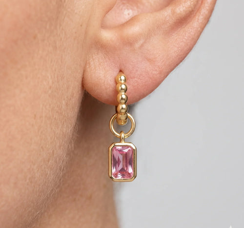Gold earring with pink gemstone worn by a person on a neutral background