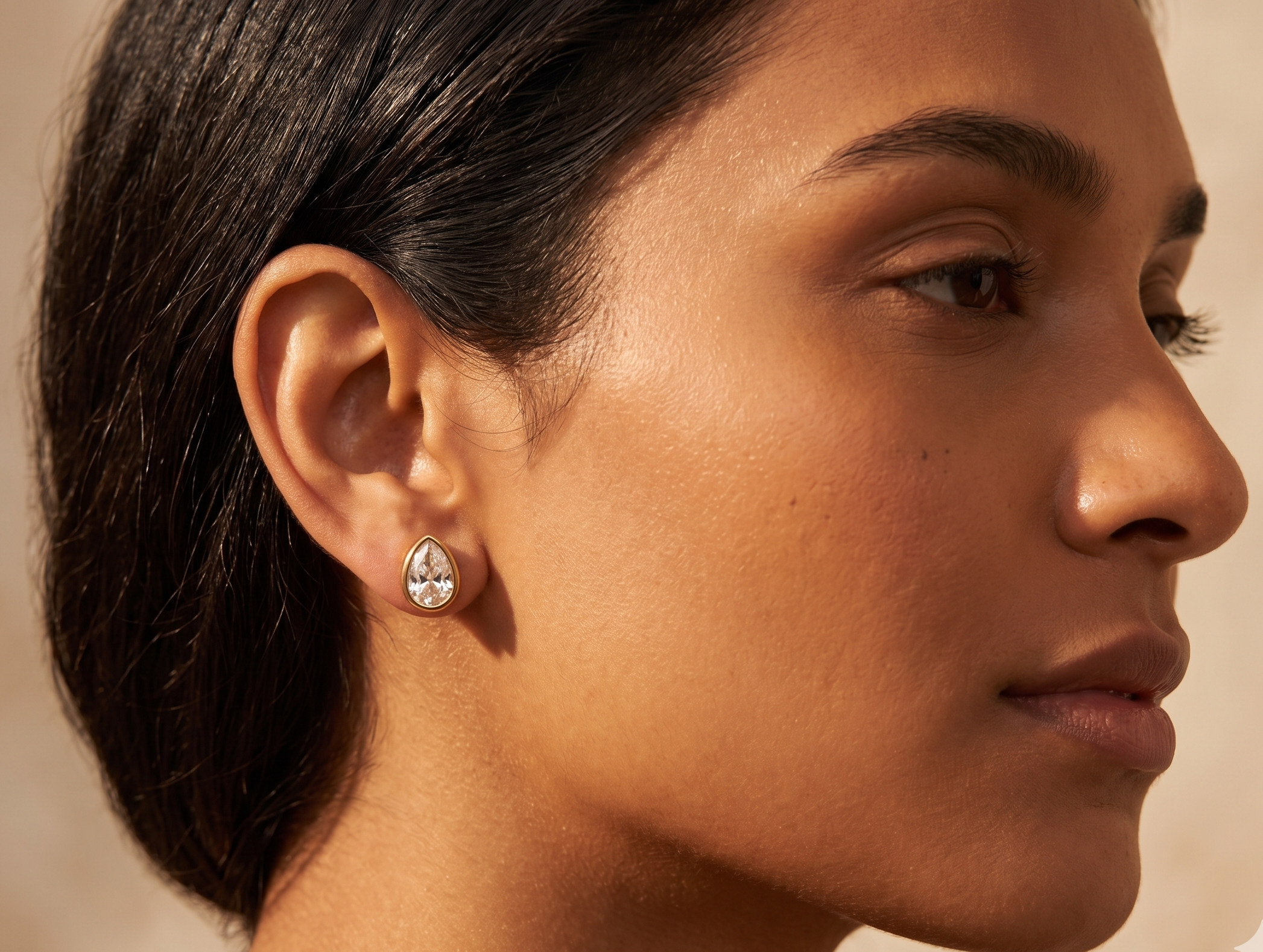 Close-up of a woman wearing a diamond earring against a neutral background