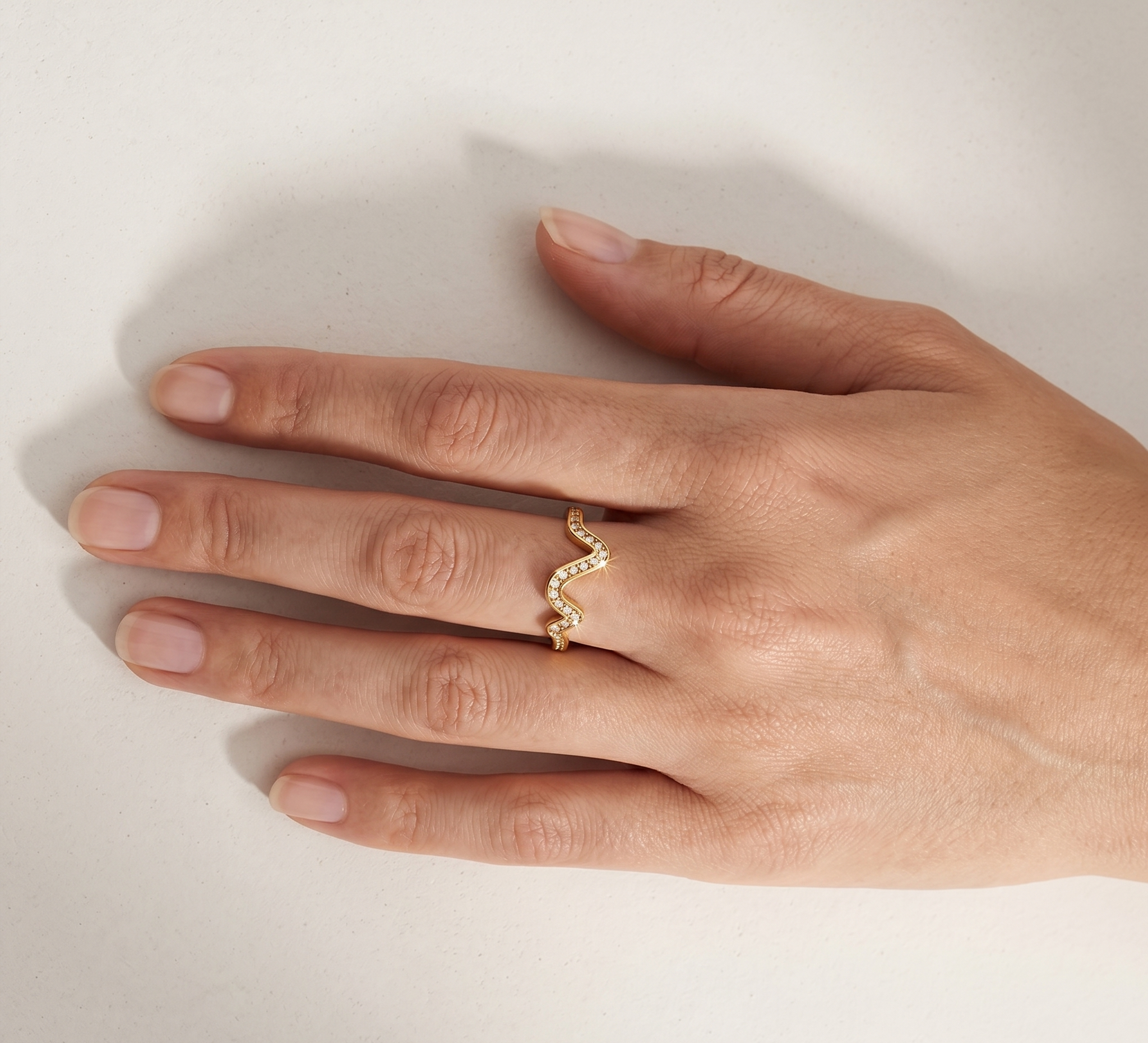Gold ring with a wavy design on a hand against a neutral background