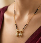 Gold necklace with black beads on a person wearing a burgundy top.