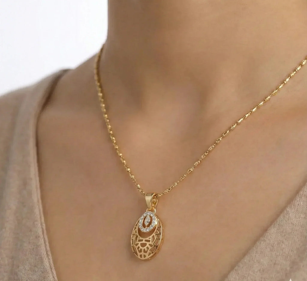 Gold necklace with a pendant on a person wearing a beige top.
