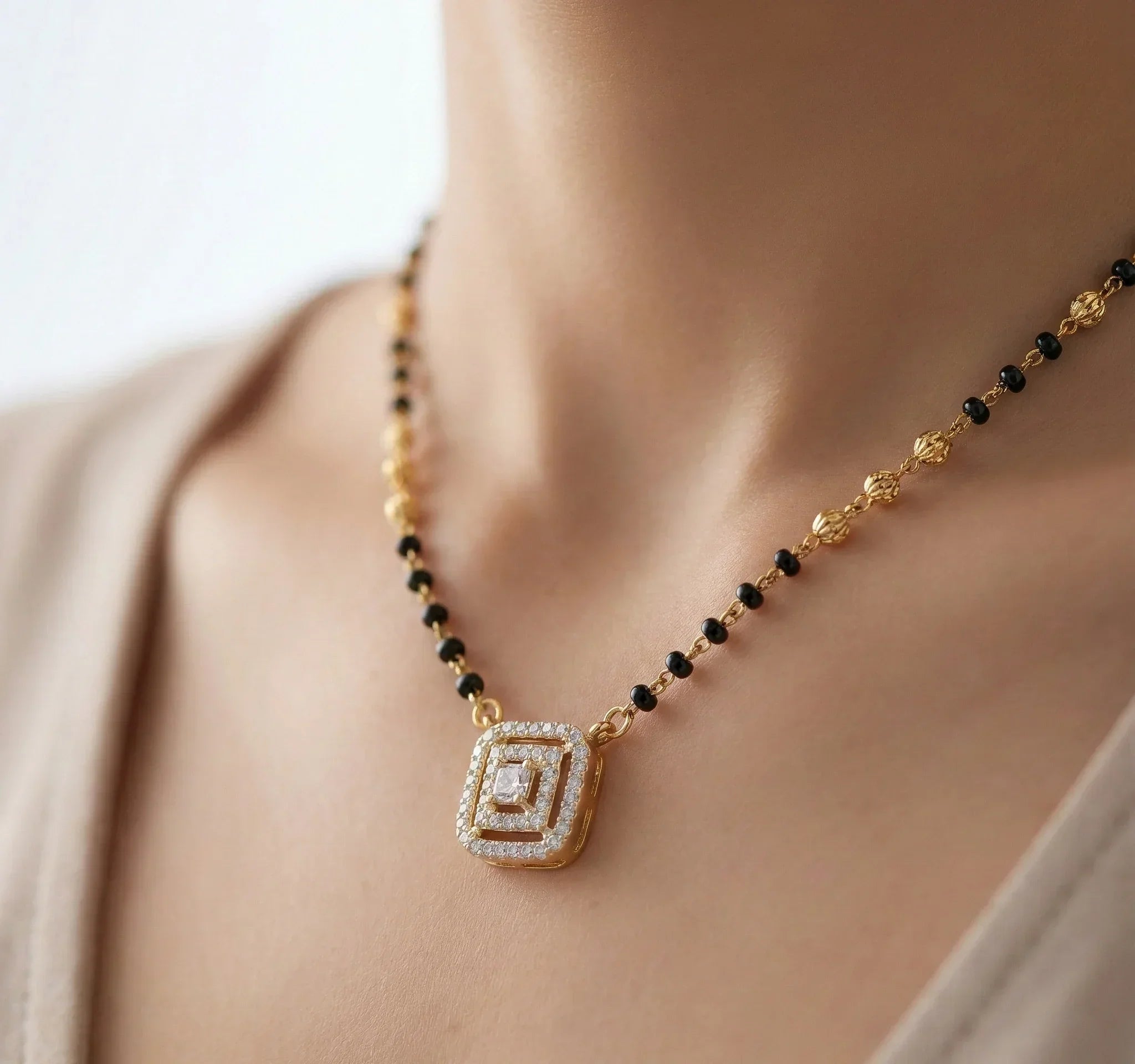 Necklace with a gold and black bead design on a person wearing a beige top.