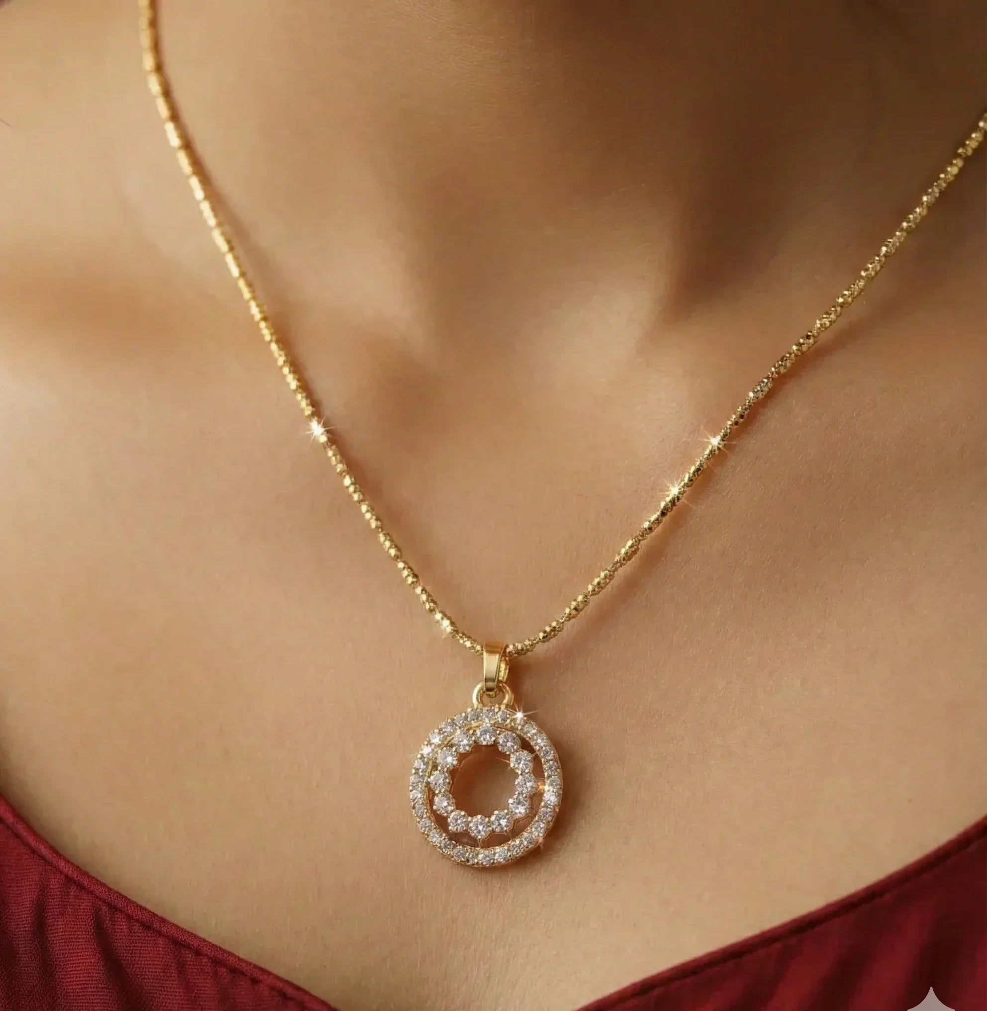 Gold necklace with a circular pendant on a person wearing a red top.