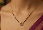 Gold necklace with black beads and a diamond pendant on a person wearing a purple saree.