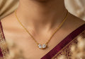 Gold necklace with a diamond pendant worn by a person in a maroon saree.