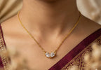 Gold necklace with a diamond pendant worn by a person in a maroon saree.