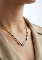 Necklace with black beads and floral pearl design worn by a person in a beige outfit.