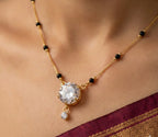 Gold necklace with a large central gemstone and smaller pendant on a person wearing a maroon saree.
