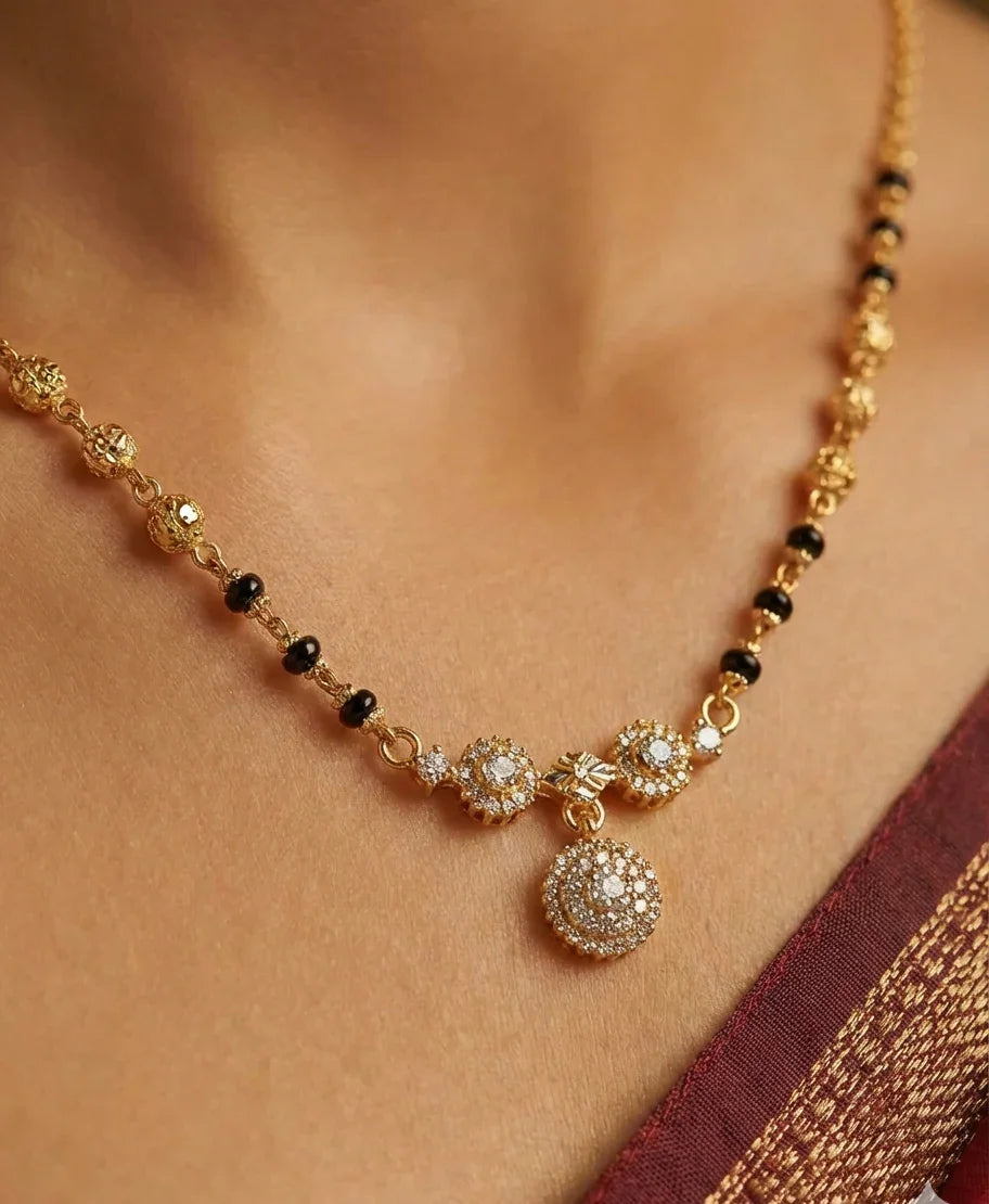 Gold necklace with black beads and decorative pendants on a person wearing a saree.