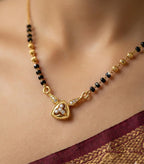 Gold necklace with black beads and a heart-shaped pendant on a blurred background