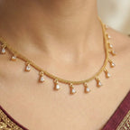 Gold necklace with diamond pendants on a person wearing a maroon saree with gold border.