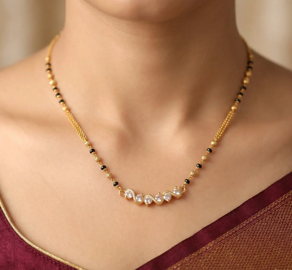 Necklace with gold chain and black beads worn by a person in a maroon top.