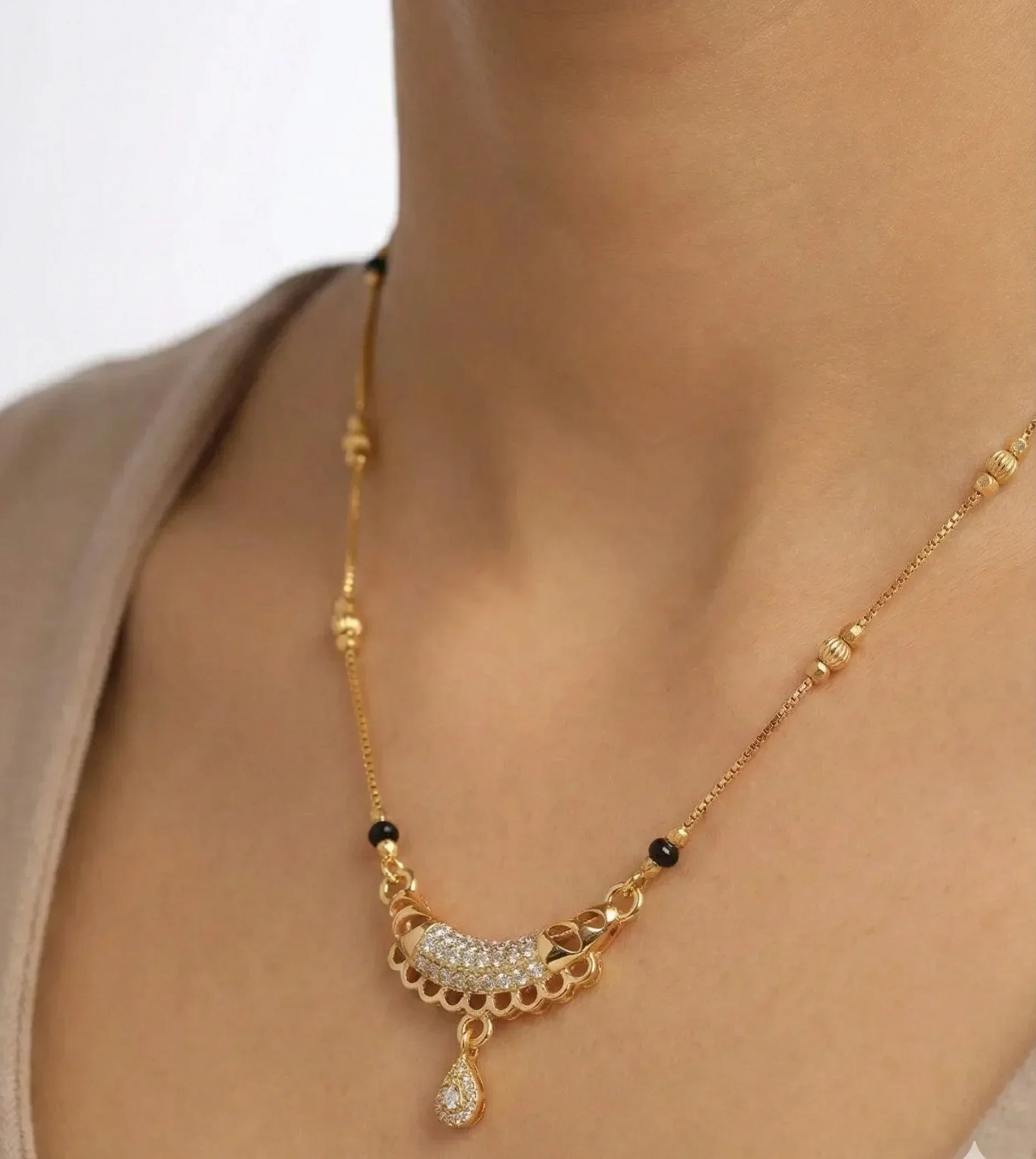 Gold necklace with a pendant on a person wearing a beige top.