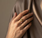 Hand wearing two rings with star-shaped designs on a draped fabric background