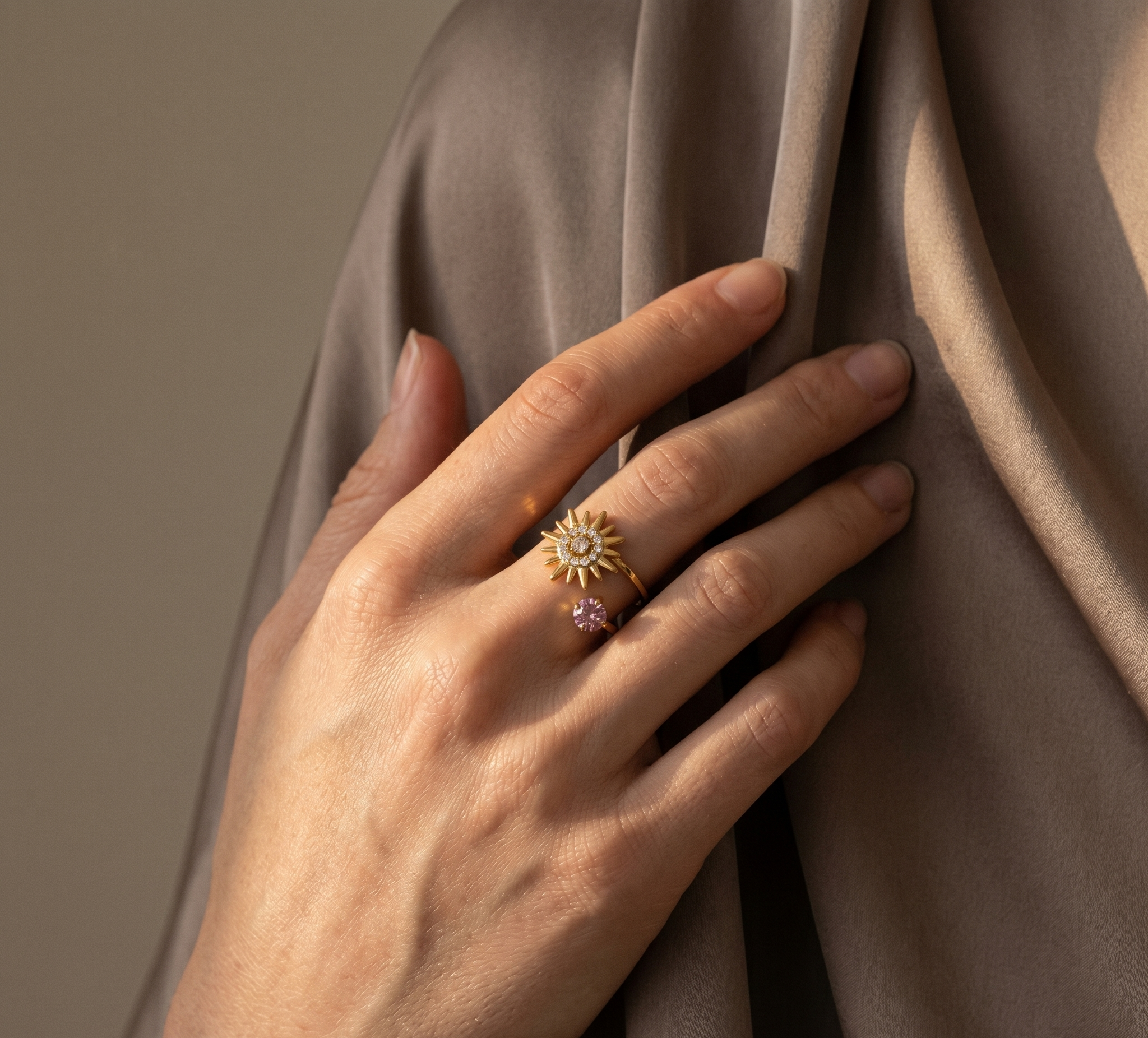 Hand wearing two rings with star-shaped designs on a draped fabric background
