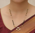 Gold necklace with black beads on a person wearing a maroon saree.