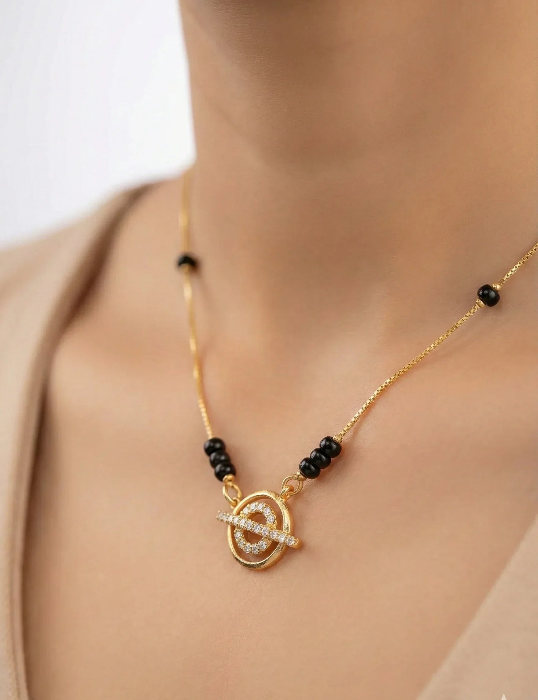Gold necklace with black beads and a circular pendant on a person wearing a beige top.