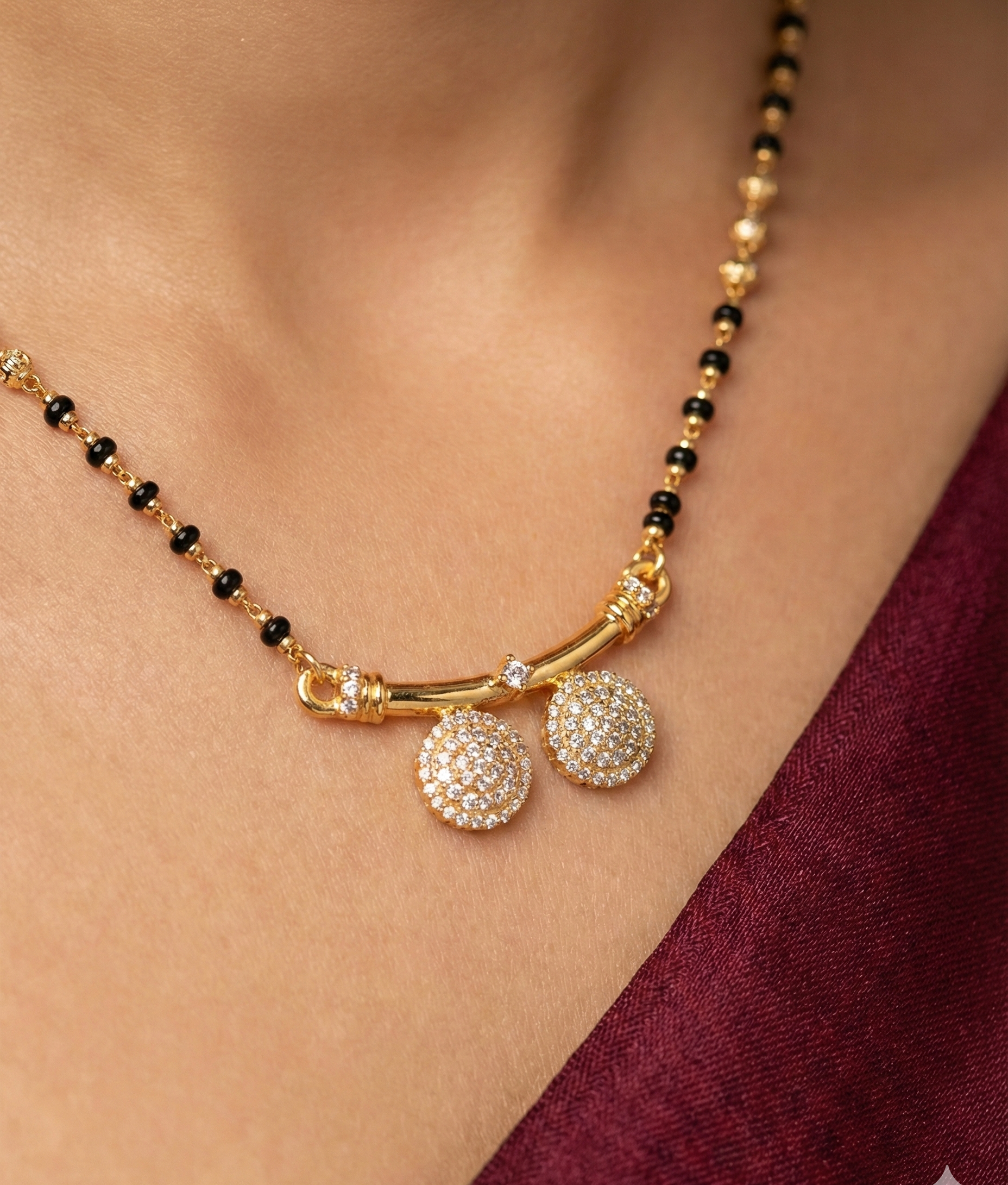 Gold necklace with black beads and decorative pendants on a person wearing a burgundy garment.