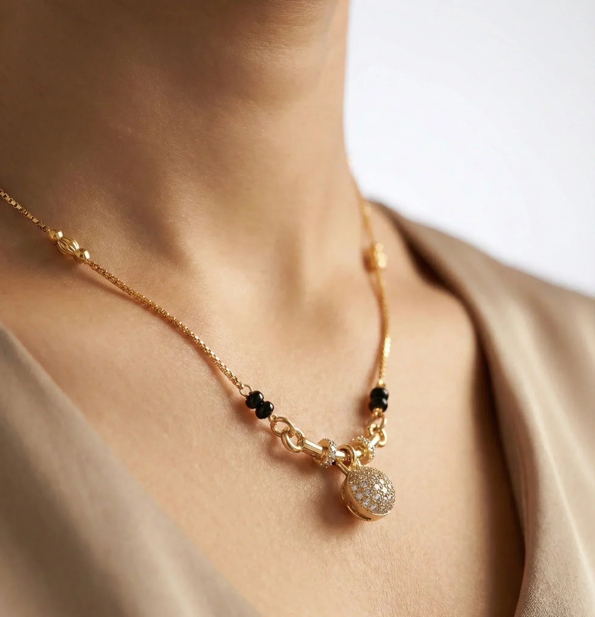 Gold necklace with a pendant on a person wearing a beige top.