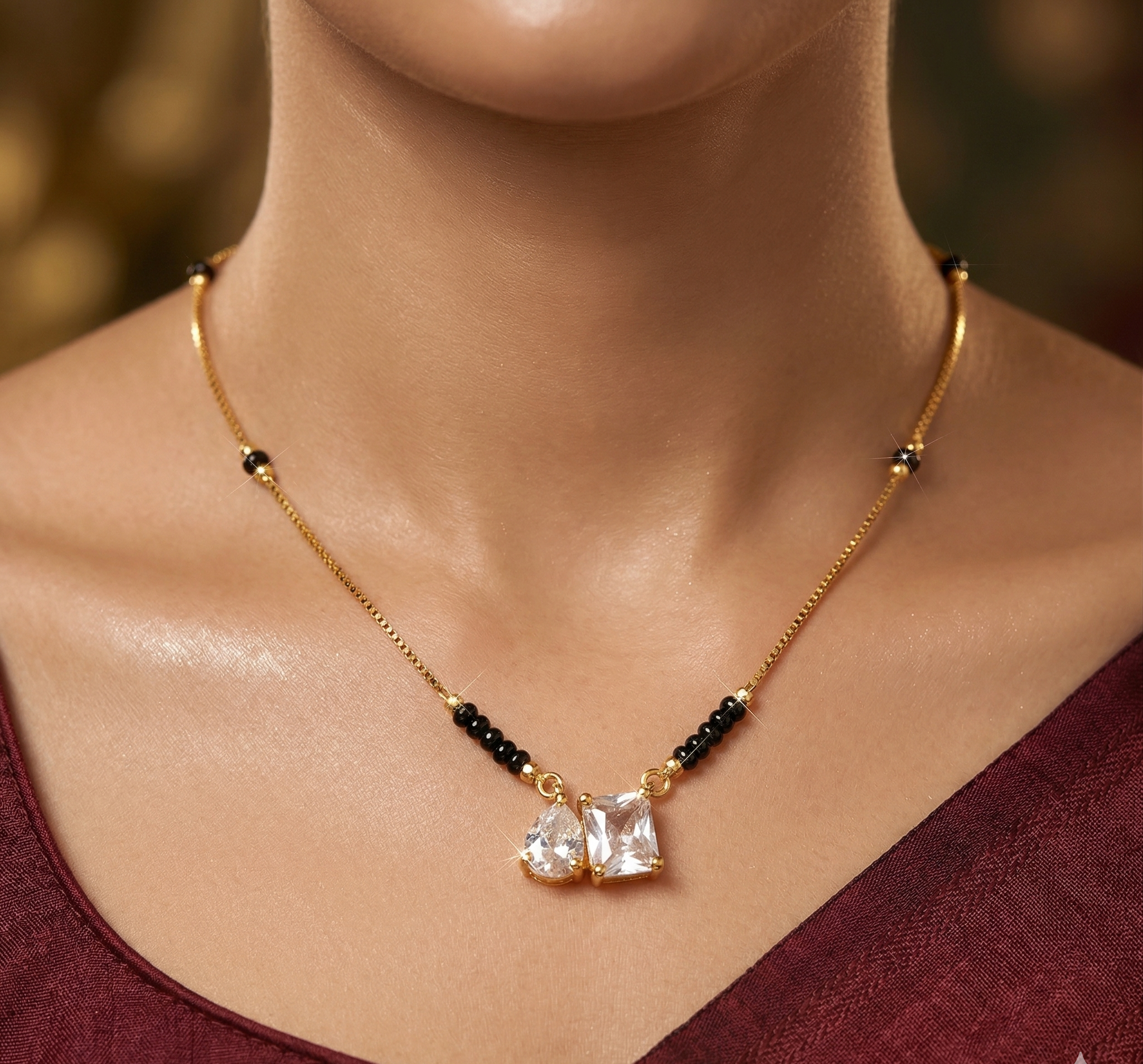 Gold necklace with black beads and clear stones worn by a person in a burgundy top.