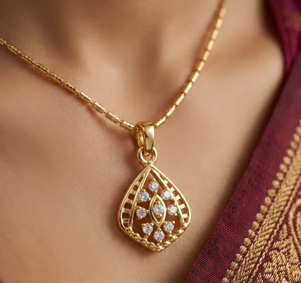 Gold necklace with a decorative pendant on a person wearing a maroon saree.