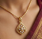 Gold necklace with a decorative pendant on a person wearing a maroon saree.