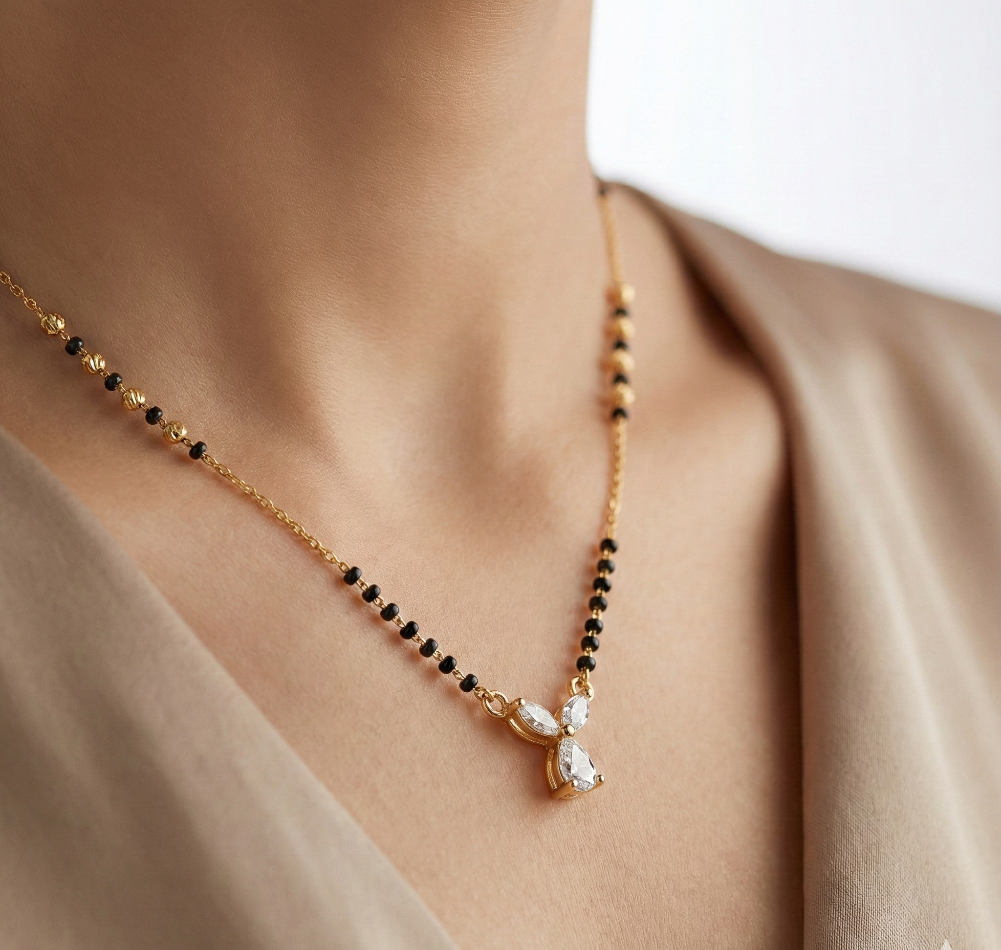 Gold necklace with black beads and a diamond pendant on a person wearing a beige top.