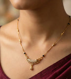 Gold necklace with black beads on a person wearing a burgundy top.