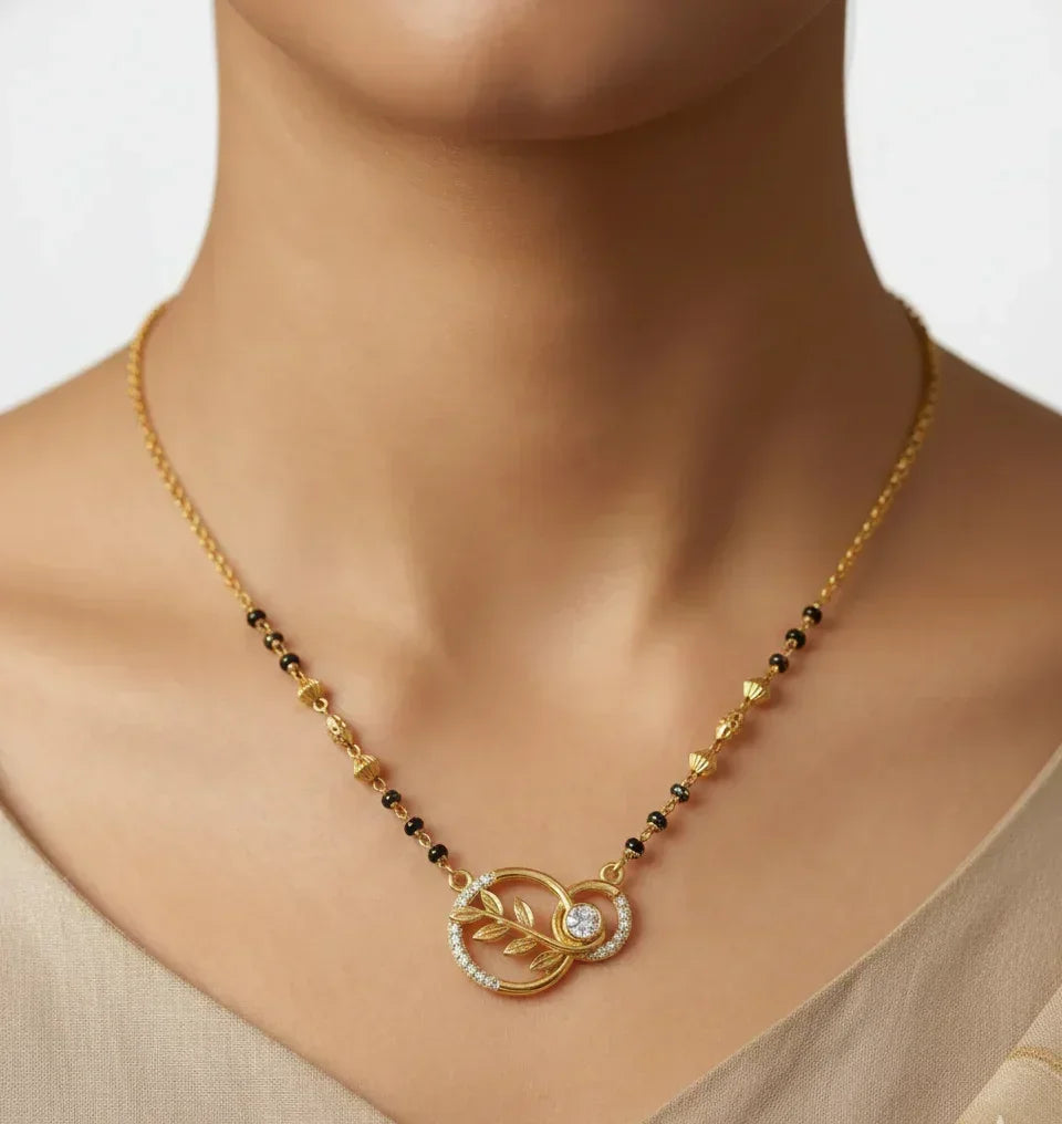 Gold necklace with a leaf design and gemstone on a neutral background